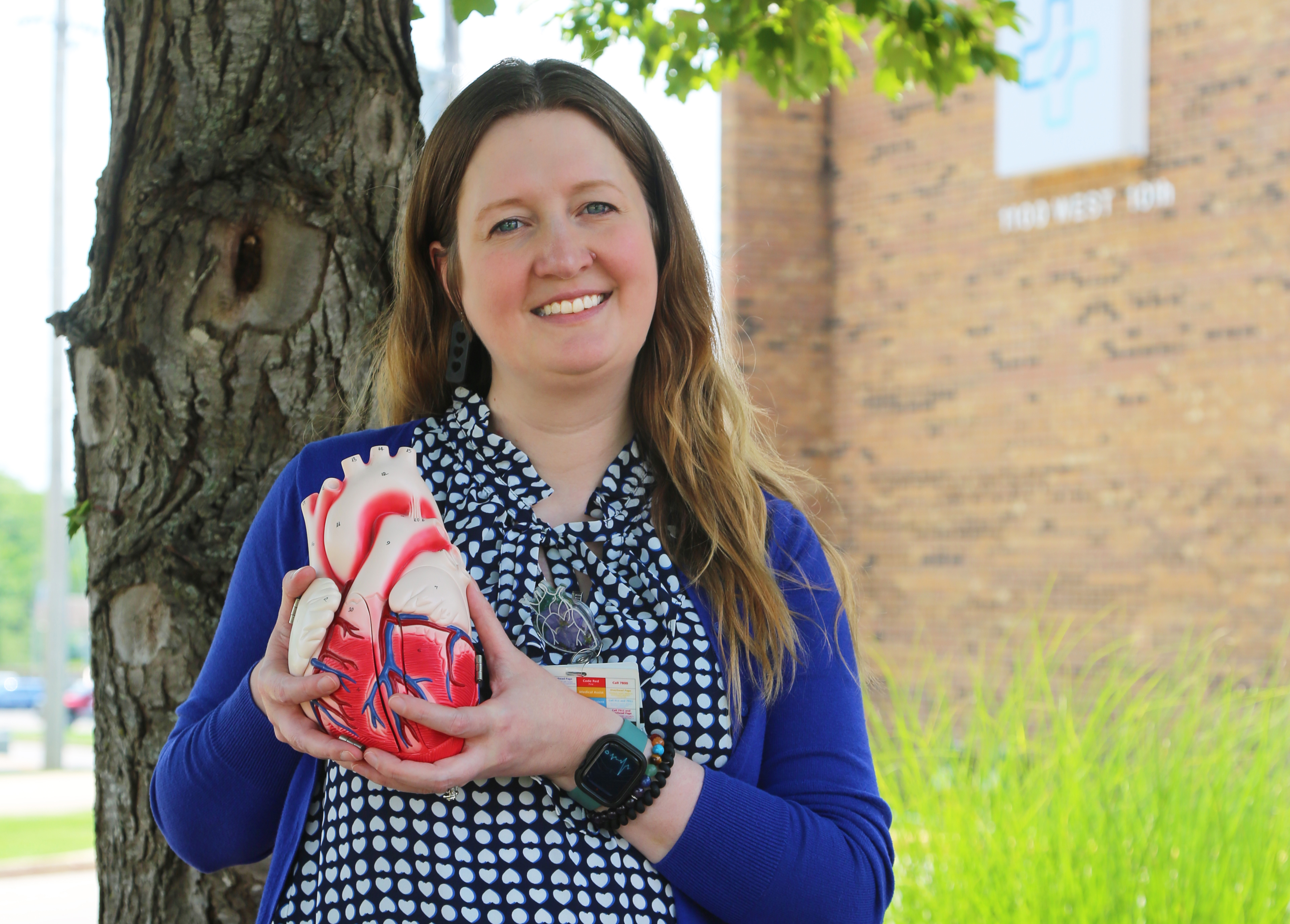Woman holding a heart model standings outside next to a tree