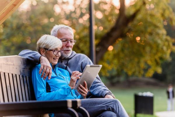 couple sitting on park bench looking at tablet