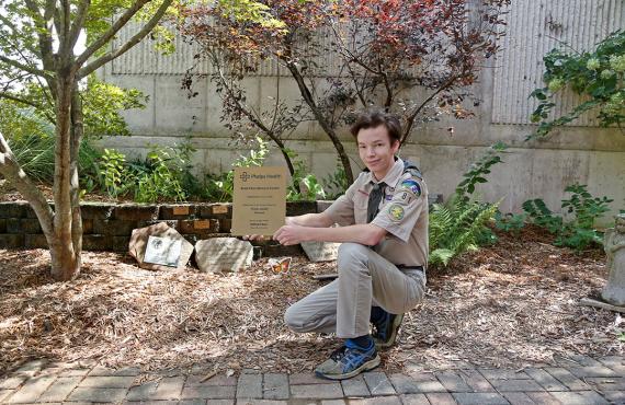 Scout WIl Baur holding a plaque in front of Bond Memorial Garden