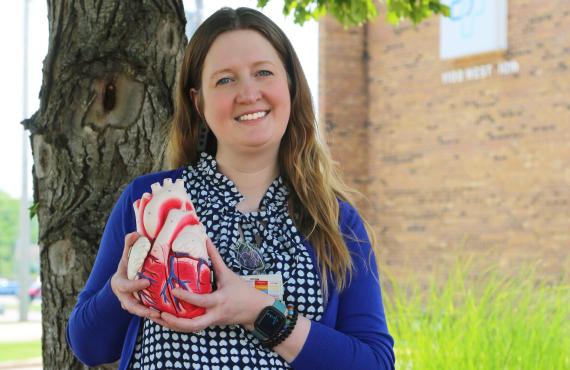 Woman holding a heart model standings outside next to a tree