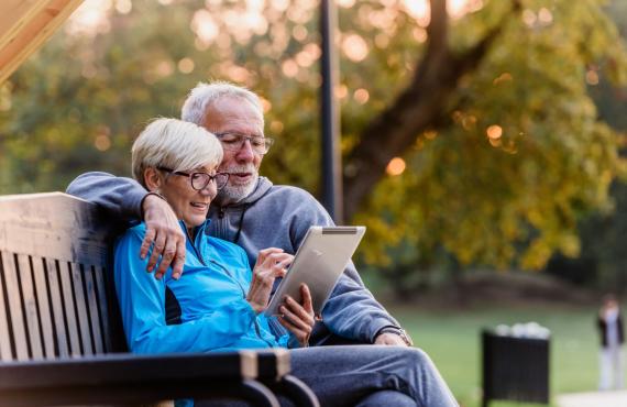 couple sitting on bench reading tablet